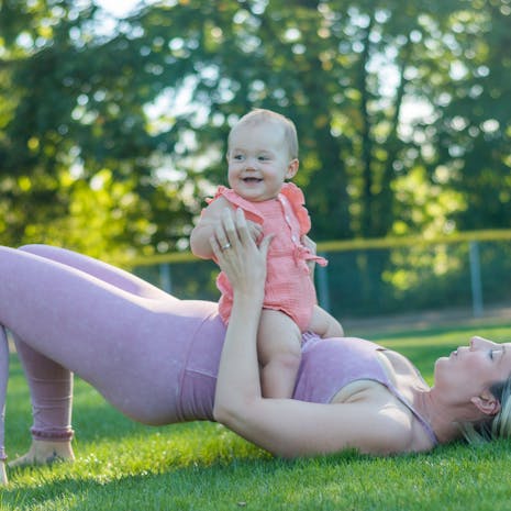 תמונה מאת Loren Castillo A mother in activewear exercises with her baby in a sunny park, promoting a healthy lifestyle.