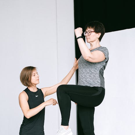 תמונה מאת Anna Shvets A senior woman working out with a fitness coach indoors, focusing on leg exercise and healthy lifestyle.