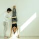 Full body of unrecognizable male instructor helping young female in activewear doing handstand in light room