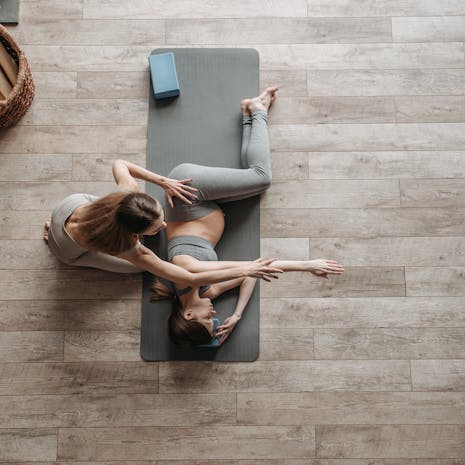 תמונה מאת Pavel Danilyuk Overhead view of a yoga instructor helping a woman stretch on a mat during an indoor session.