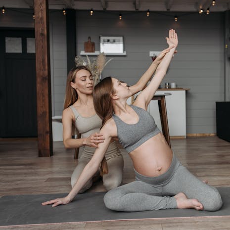 תמונה מאת Pavel Danilyuk Pregnant woman on yoga mat with instructor, focusing on prenatal exercise.