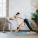 Yoga instructor guides student in downward dog pose during indoor session.